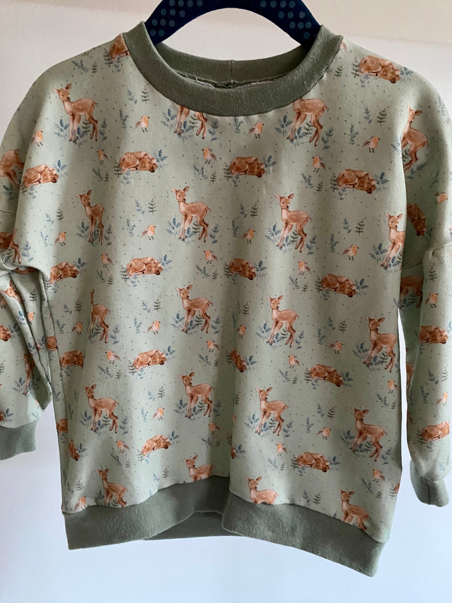 Genähter Pullover mit Reh und Vogel Motiv auf grünem Hintergrund.
